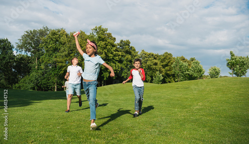 Cute happy multiethnic kids playing together and running on green meadow in park