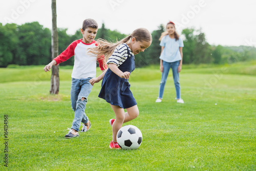 Adorable cheerful children playing soccer with ball on green grass