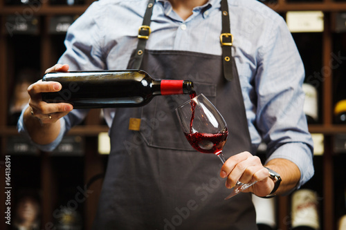 Konstfotografi Male sommelier pouring red wine into long-stemmed wineglasses.
