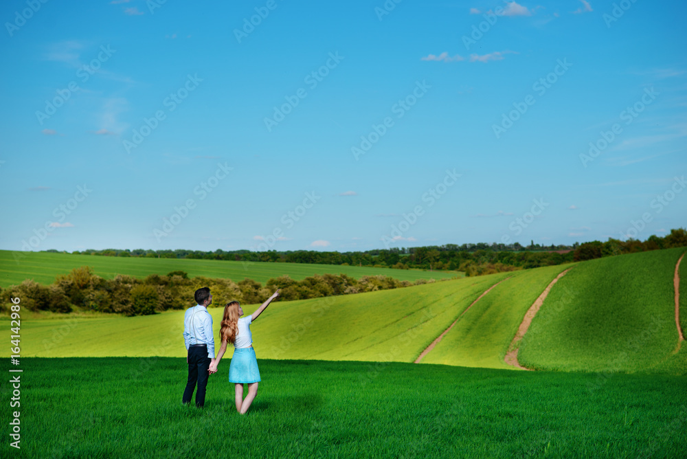 A young couple standing in the field, the girl shows her hand to the sky A young couple standing in the field, the girl shows her hand to the sky