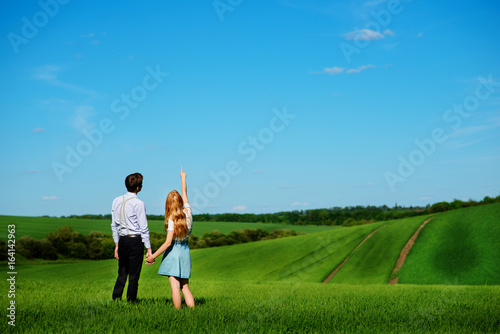 A young couple standing in the field  the girl shows her hand to the sky