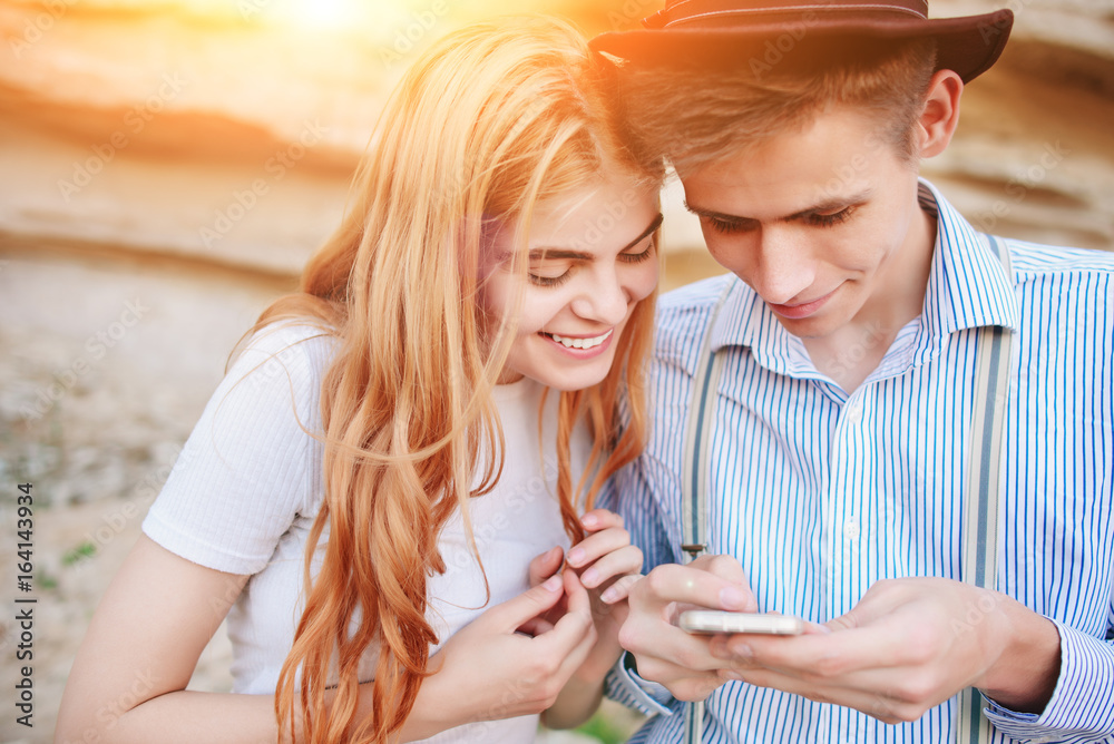 Attractive man and beautiful woman are looking at the screen of a smartphone on the background of a sand quarry Attractive man and beautiful woman are looking at the screen of a smartphone on the background of a sand quarry