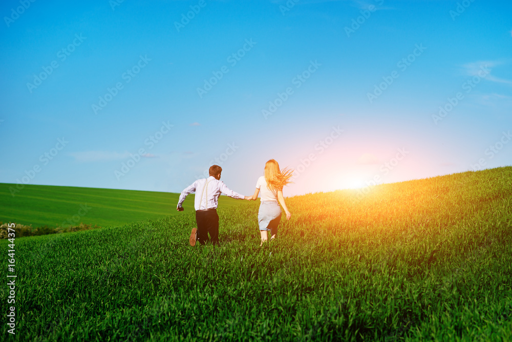 Young happy lovers running on meadow with green grass and blue sky, From the back Young happy lovers running on meadow with green grass and blue sky, From the back
