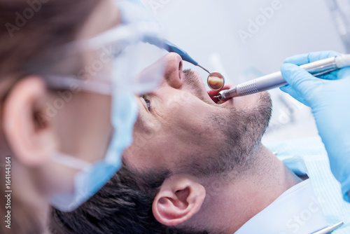 dentist in protective mask and glasses curing teeth of patient