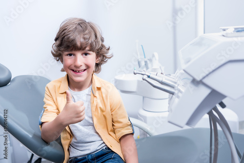 portrait of little smiling boy showing thumb up in dental clinic