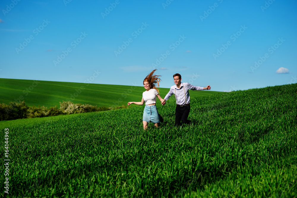Young happy lovers running on meadow with green grass and blue sky Young happy lovers running on meadow with green grass and blue sky