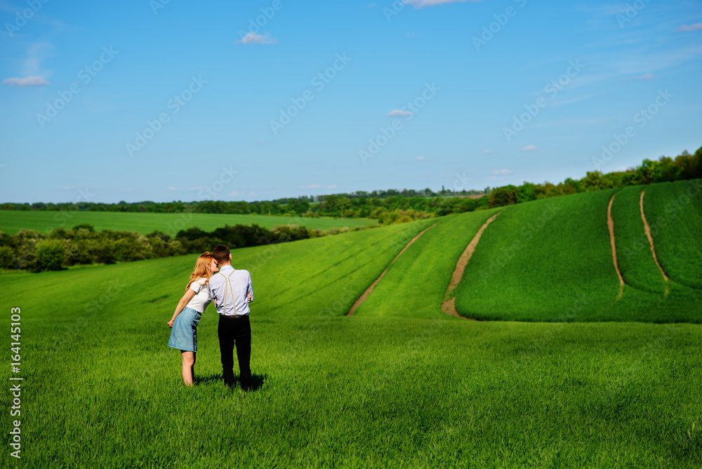 A young couple standing in the field, the girl kisses the boy in the cheek A young couple standing in the field, the girl kisses the boy in the cheek