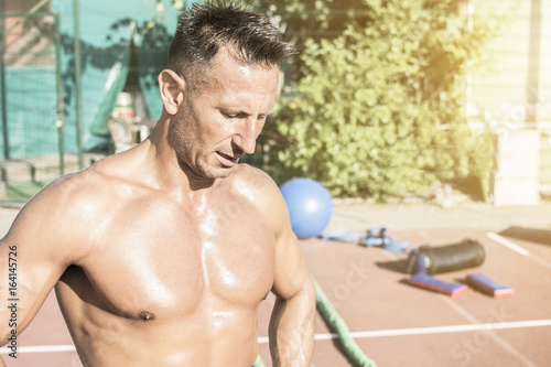 Handsome middle aged man working out on a running track. Healthy adult man sun baiting. Tanned skin and shirtless middle-aged man.
