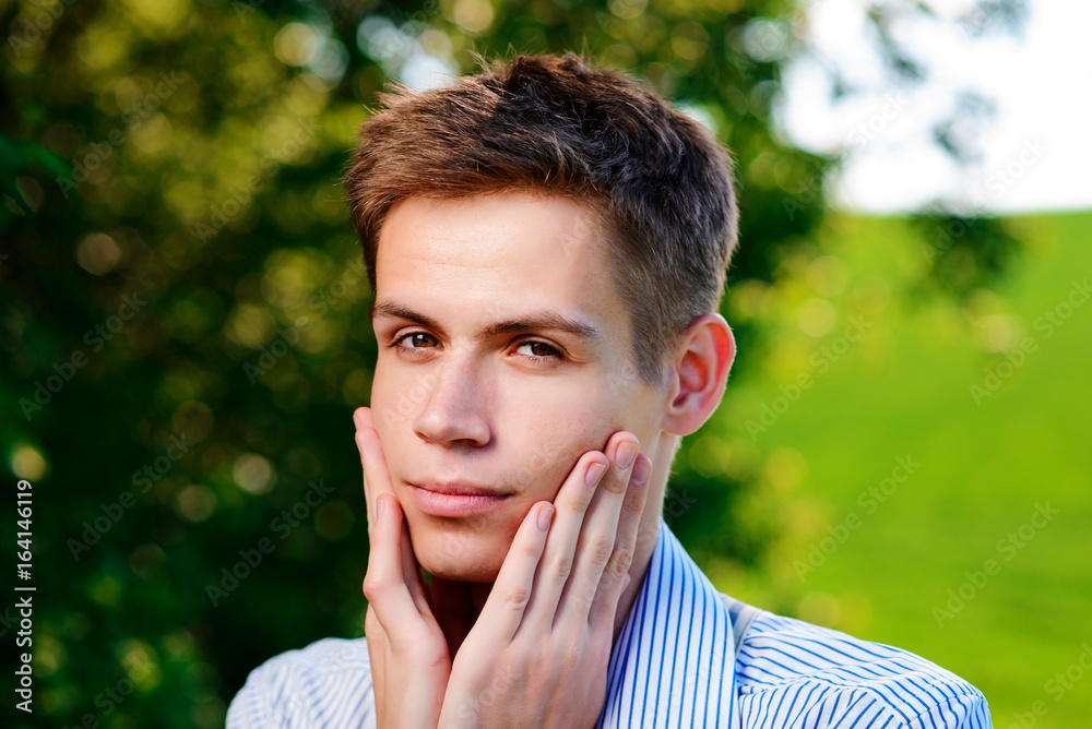 On the background of nature, a beautiful man looking into the camera holds his hands around his neck and face On the background of nature, a beautiful man looking into the camera holds his hands around his neck and face