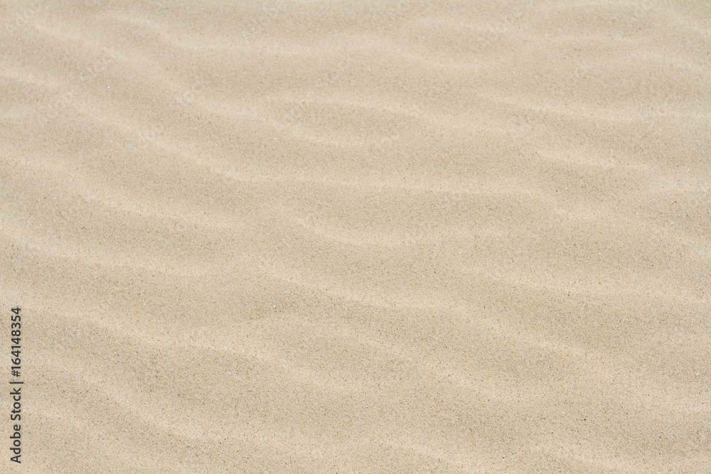 A full frame, background image of the surface of a sandy beach with soft, rippled effect sand that is light brown in colour. A full frame, background image of the surface of a sandy beach with soft, rippled effect sand that is light brown in colour.