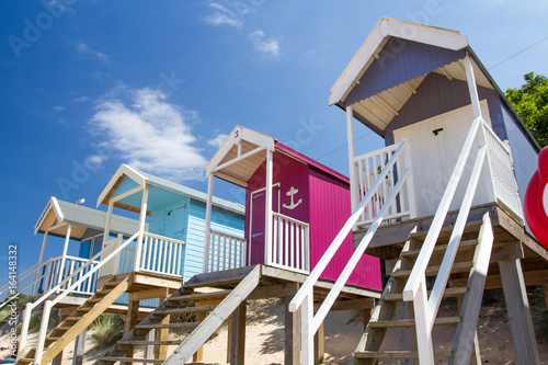 Rows of colourful wooden beach huts on a sandy beach in Norfolk, UK under a blue sky and summer sunshine. photo