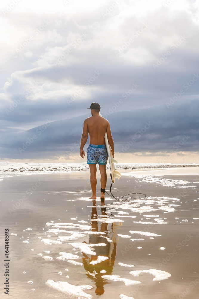 Handsome man stand with surfing board at surf spot at sea ocean beach and wait for wave. View from back. Concept of sport, fitness, freedom, happiness, new modern life, hipster, generation Y.