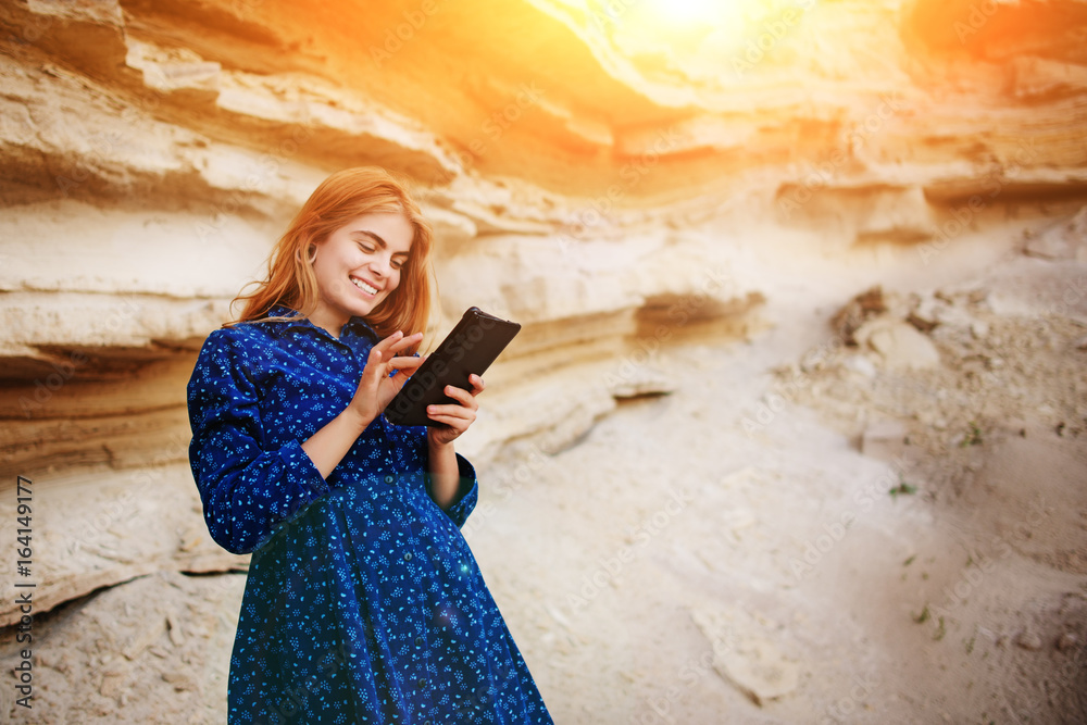 Beautiful woman smiling and looking at the screen of a tablet on the background of a sand quarry Beautiful woman smiling and looking at the screen of a tablet on the background of a sand quarry