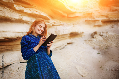 Beautiful woman smiling and looking at the screen of a tablet on the background of a sand quarry