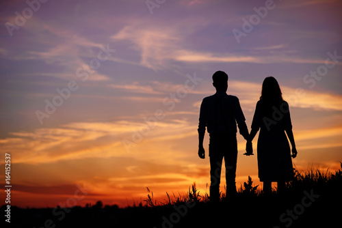 young couple is holding hands on a background sunset silhouette