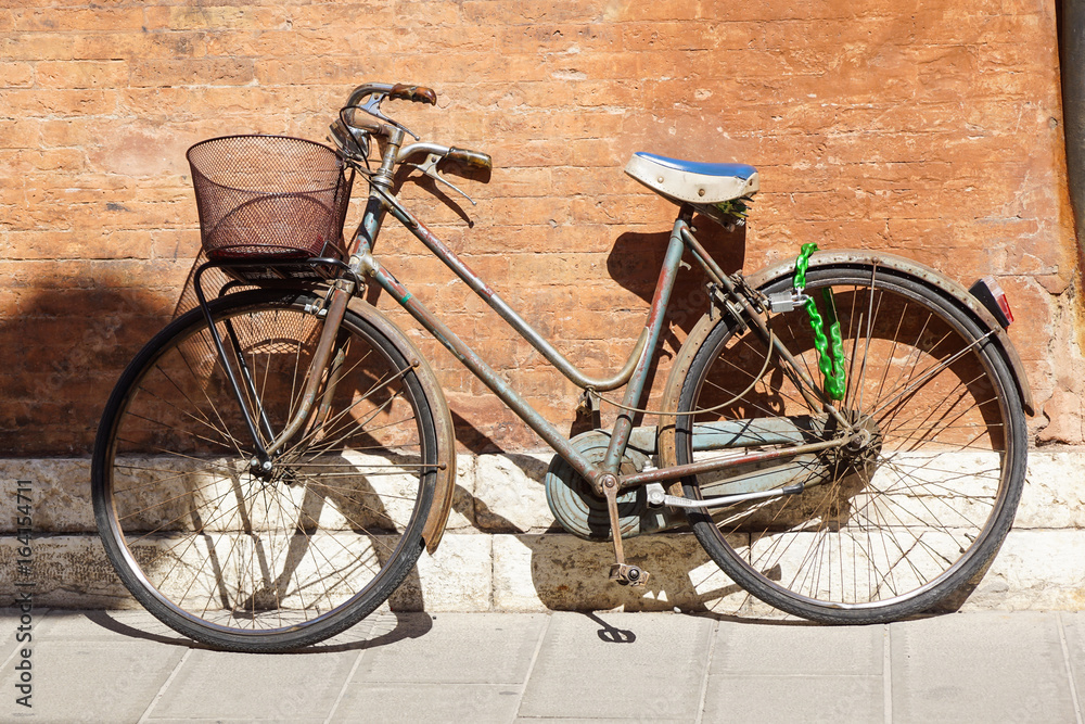 An old, rusty white bicycle with a basket leaning against a grungy wall in Italy.