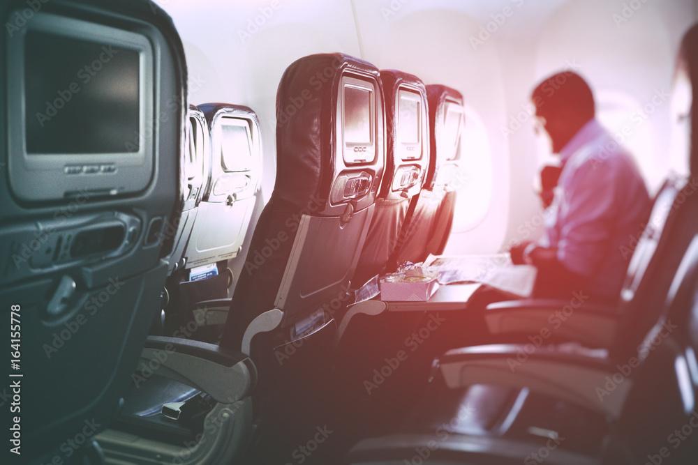 Fototapeta premium Blurry image of airplane interior with incidental passenger sitting on seats - travel concept, retro styled.