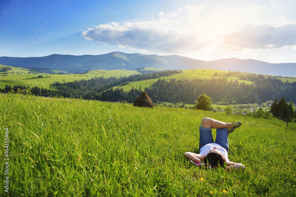 Woman lies on a meadow in the mountains in the grass in summer