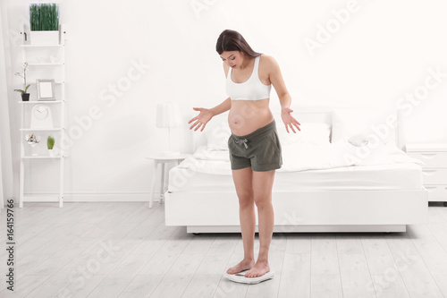 Pregnant woman standing on scales at home. Pregnancy weight gain concept