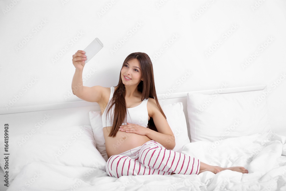 Pregnant woman with mobile phone sitting on bed Pregnant woman with mobile phone sitting on bed