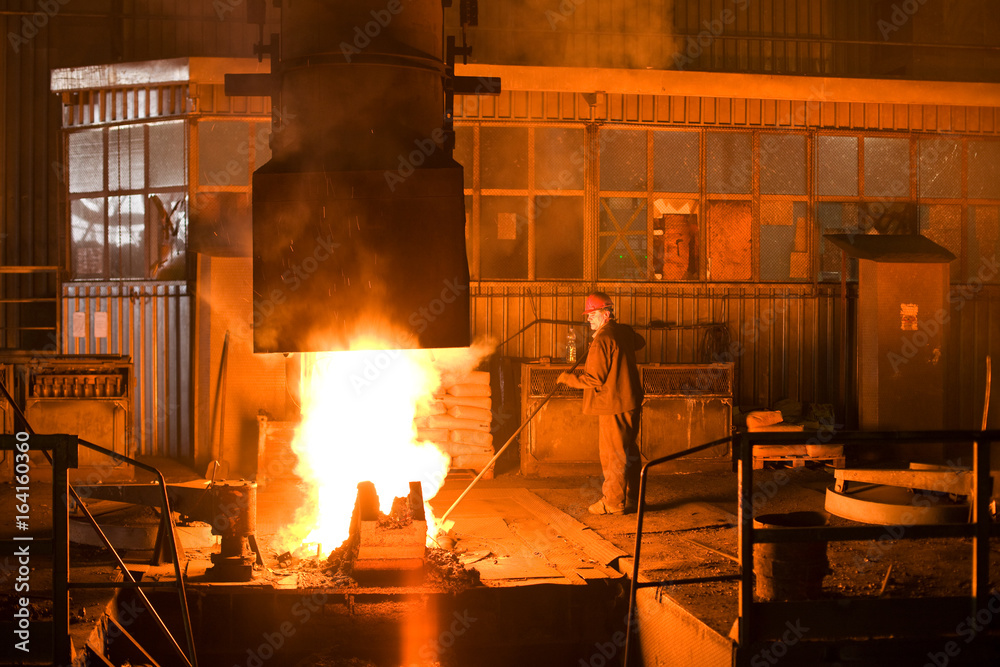 Working in a foundry. Worker looking down, red color is a reflection of the molten metal. Very high heat and purple fringing. See more images and video from this series.