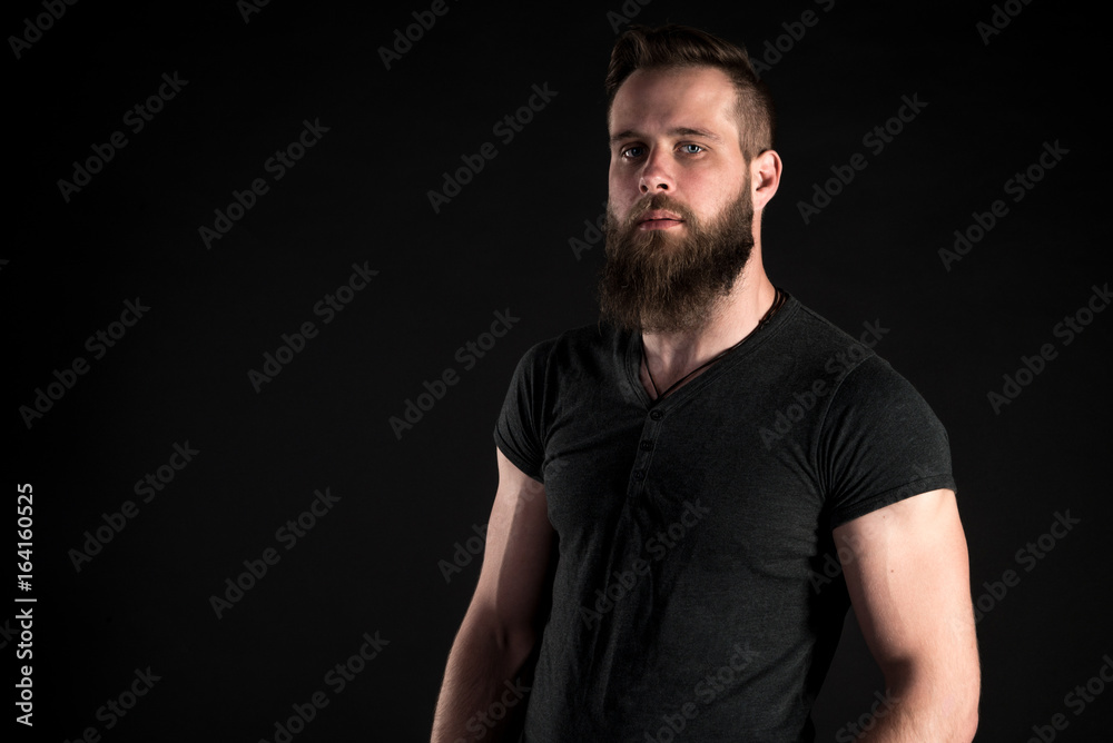 A charismatic and stylish man with a beard stands full-length on a black isolated background. Horizontal frame