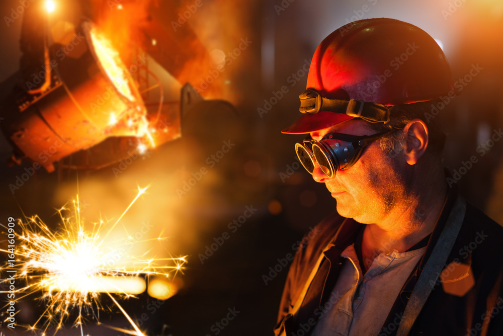 Foundry worker looking at sparks in the front of the molten steel. Foundry worker looking at sparks in the front of the molten steel.