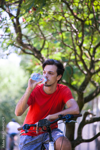 young man sit on bike in wood resting drink water