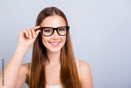 Happy young girl is in a stylish glasses, wearing casual singlet, holding her eyewear, smiling on pure light background
