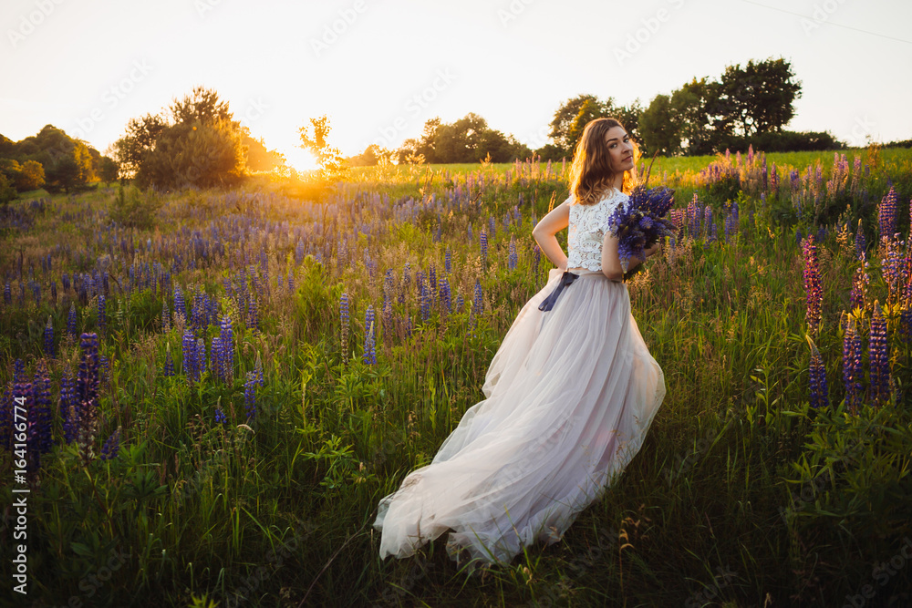 Stunning lady in white dress stands with bouquet on the field