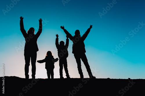 Silhouettes of family with two kids hiking at sunset