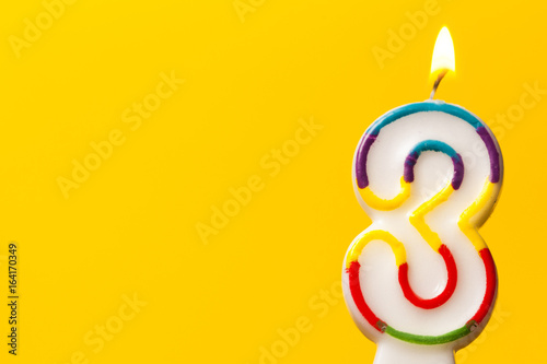 Number 3 birthday celebration candle against a bright yellow background