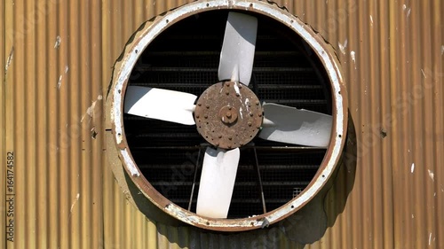 Old rusty industrial ventilation fan turning slowly in a side wall of a factory unit photo