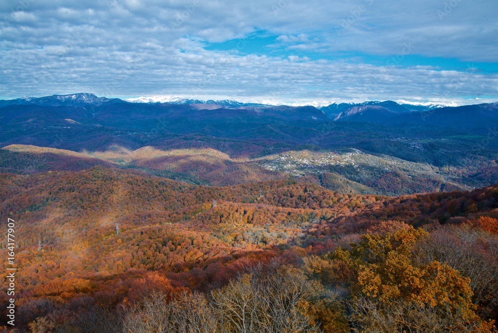 Landscape in autumn colors. Caucasian mountains, autumn forest and blue sky with clouds