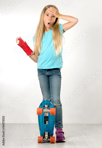 junges Mädchen mit Gipsarm hält sich erschreckt die Hand an den Kopf und steht auf Skateboard