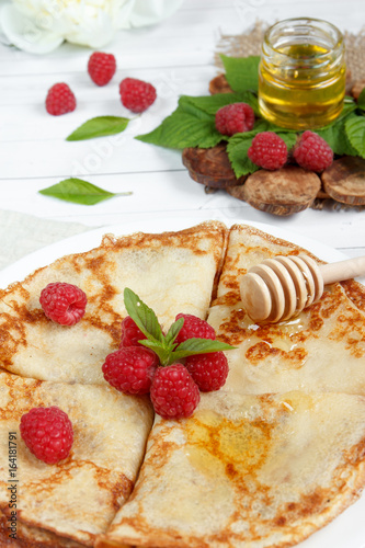 Thin pancakes with honey and raspberries on a white plate photo