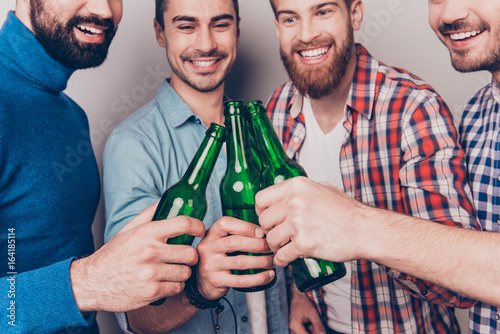 Cheers men! Bachelor men`s life. Low angle cropped photo of four happy friends, clinking their glasses of beer. They are fans of sports games as football, basketball, hockey, baseball photo