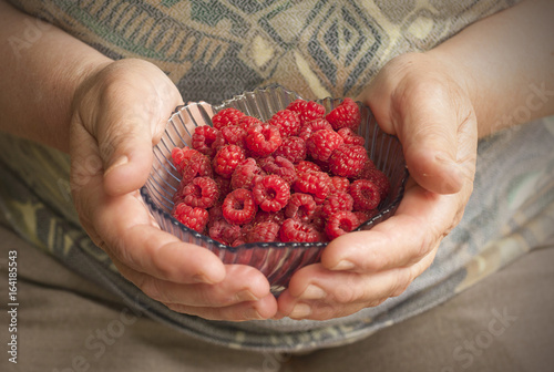 Woman hand holding a glass plate with raspberries