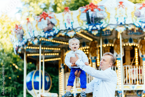 Happy father throwing his son high in front of carousel in amusement park