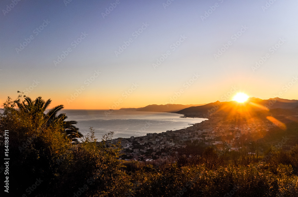 Stunning ligurian coastline at sunset as seen from Borgio Verezzi - Liguria, Italy. Evening scene shortly before sunset with the ocean, mountains in the background and a palm tree in the foreground.