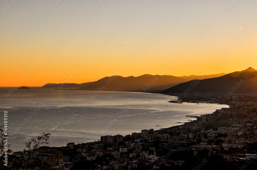 Stunning ligurian coastline at sunset as seen from Borgio Verezzi - Liguria, Italy. Evening scene shortly after sunset with the ocean, mountains in the background and a bush in the foreground.