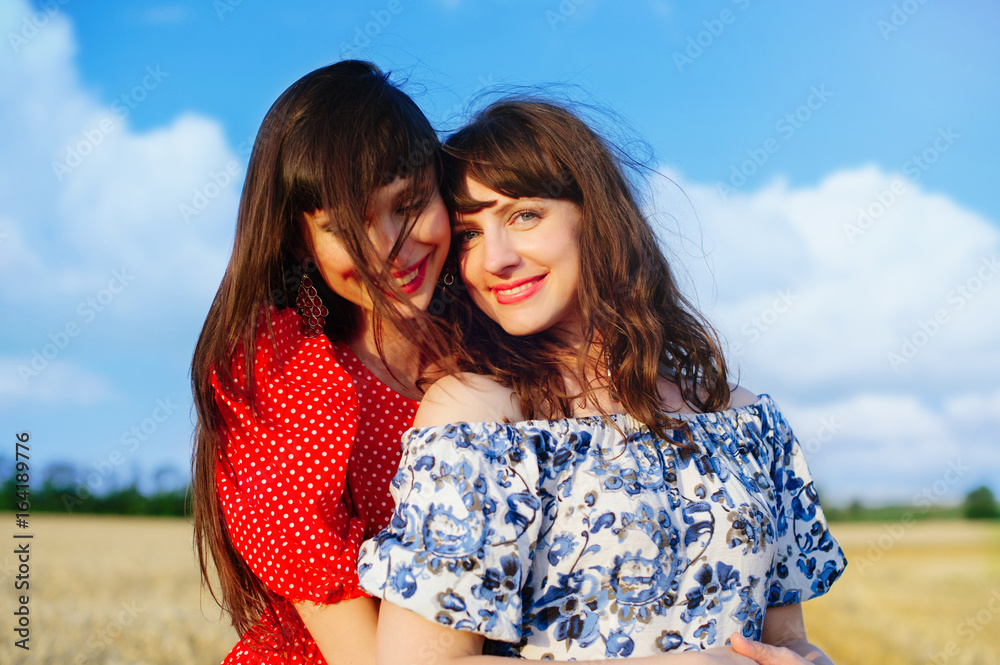 Two cheerful women in a wheat field at sunset in a blue and red long air dress. Two cheerful women in a wheat field at sunset in a blue and red long air dress.