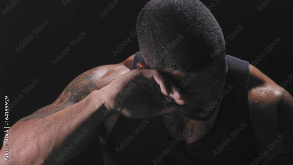Muscular black man wiping the sweat off his forehead and staring at the camera on a dark background