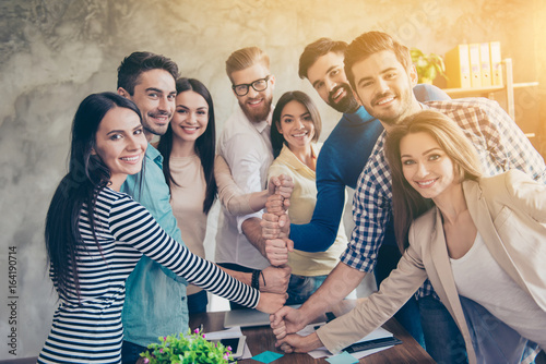 Conception of successful team-building. Close up of businesspeople putting their fists on top of each other on the desktop in nice light workstation, wearing casual clothes