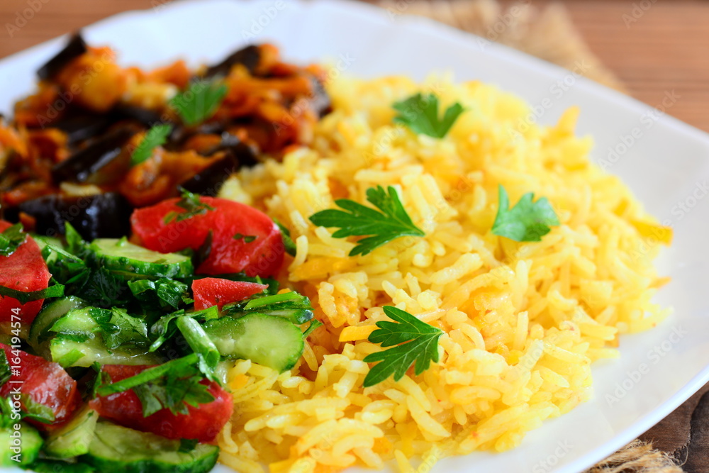 Vegetable rice, eggplant ragu, tomatoes and cucumber salad on a white plate and a brown wooden table. Healthy and delicious vegetarian recipe idea. Closeup Vegetable rice, eggplant ragu, tomatoes and cucumber salad on a white plate and a brown wooden table. Healthy and delicious vegetarian recipe idea. Closeup