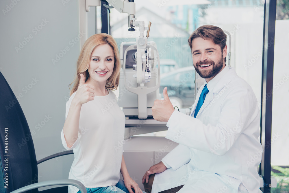 Obraz premium Healthcare, people, eyesight and vision concept. Smiling man optician in white coat and a blond woman patient are showing thumbs up gesture at optics store
