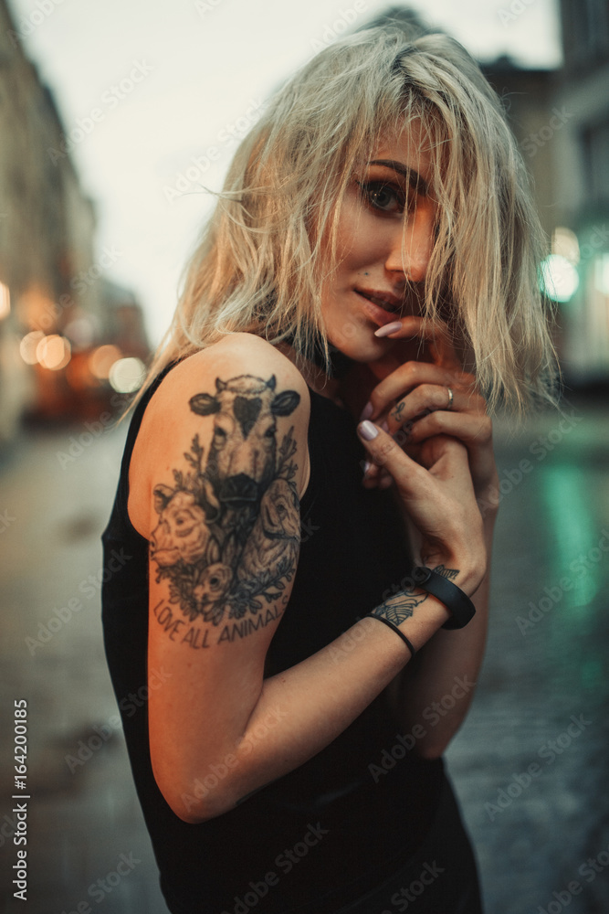 Φωτογραφία Young woman portrait with tattoo on shoulder standing on city street in evening
