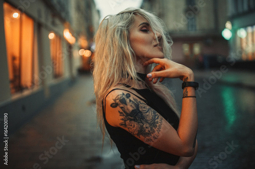 Young woman portrait with tattoo on shoulder standing on city street in evening. photo