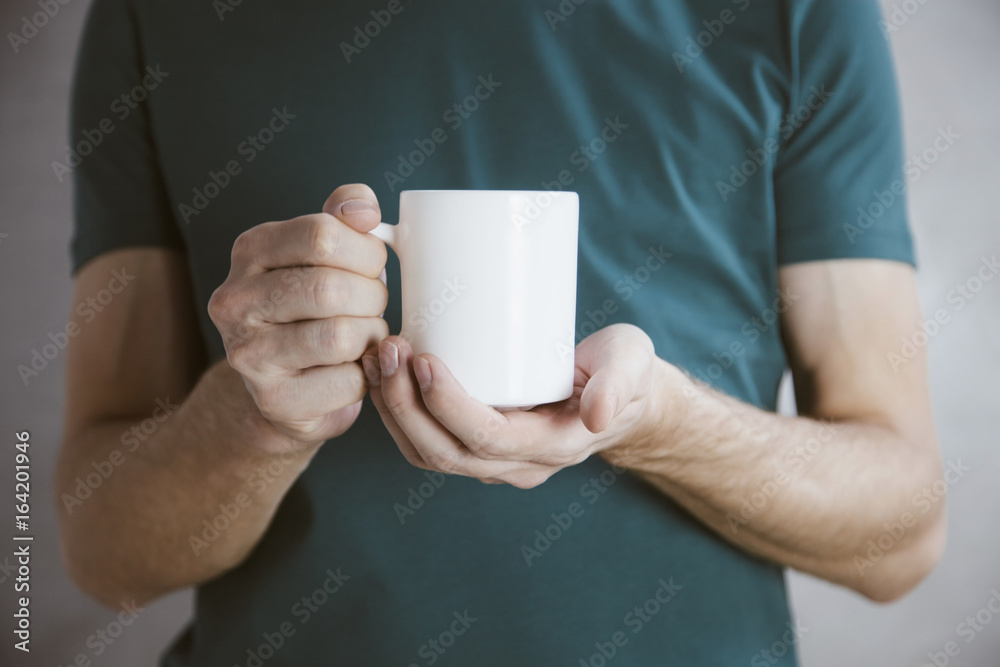 Man in green t-shirt holding big white coffee cup.Mock up of clean coffee cup.Horizontal mockup. Man in green t-shirt holding big white coffee cup.Mock up of clean coffee cup.Horizontal mockup.