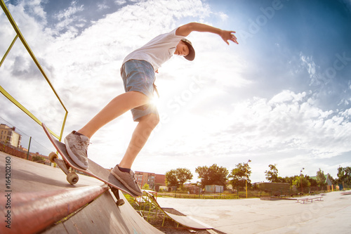 Teenager skater in a cap and shorts on rails on a skateboard in a skate park